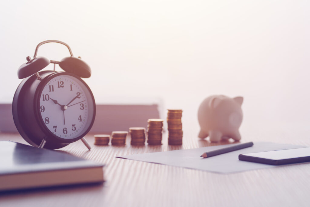 Savings, finances, economy and home budget calculations. Vintage clock, piggy bank and coins stacked on home desk.